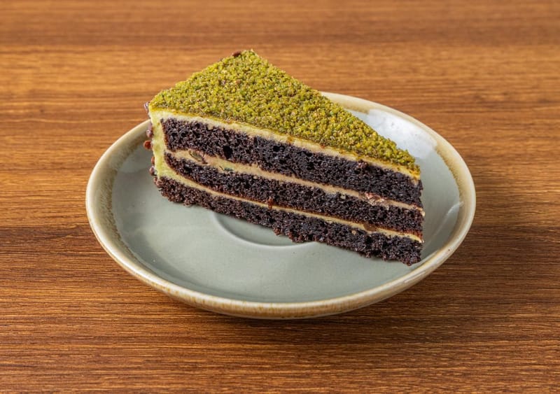 A slice of three-layer chocolate cake with a green crumb topping on a sage plate