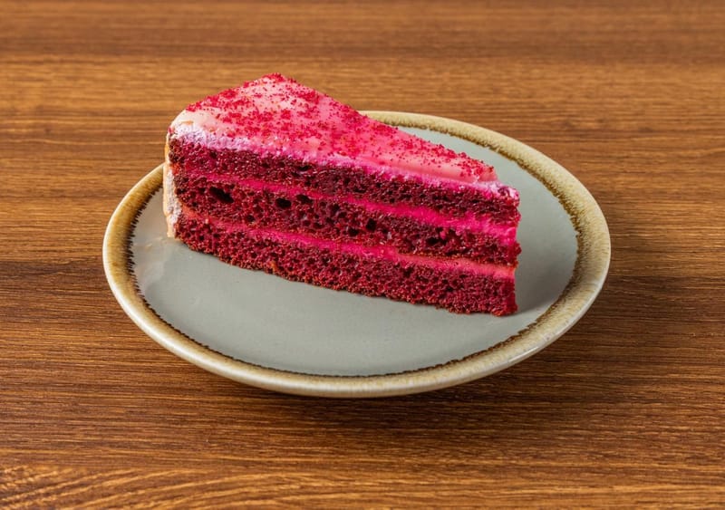 A slice of red velvet layer cake with pink frosting and a red crumb on a sage plate