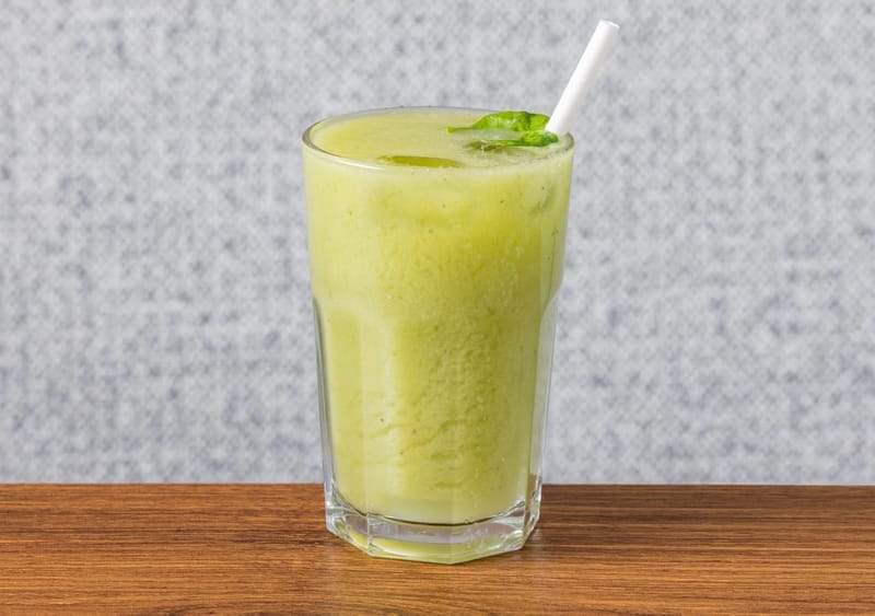 Green Detox smoothie in a tall glass with a fresh leaf and a paper straw