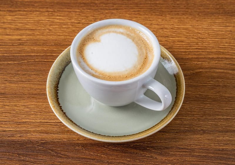 A milky coffee with a heart of foam in a white cup on a sage saucer