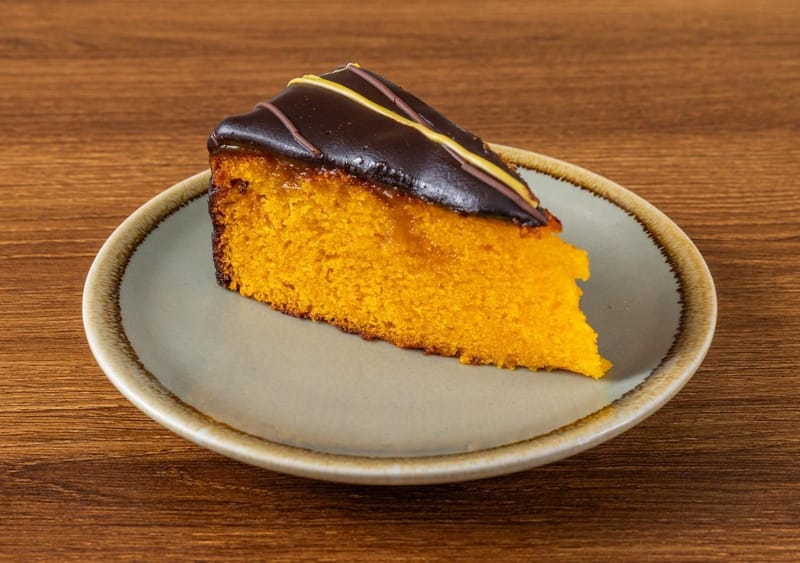 A slice of golden sponge cake with a glossy chocolate topping on a sage plate