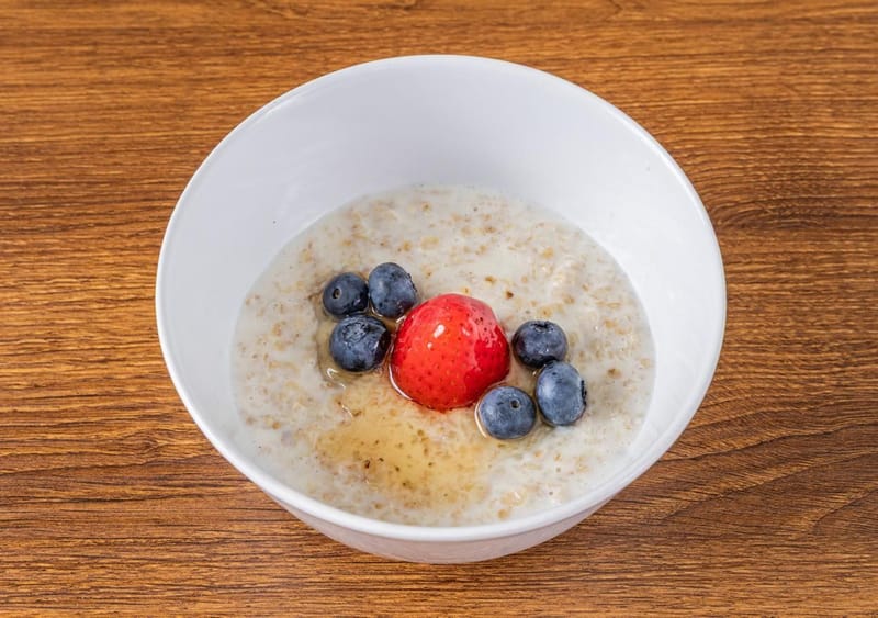 A bowl of oat porridge topped with a strawberry, blueberries and a drizzle of honey