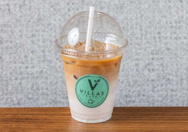 Iced coffee with milk over ice in a Villas Cafe takeaway cup with a paper straw