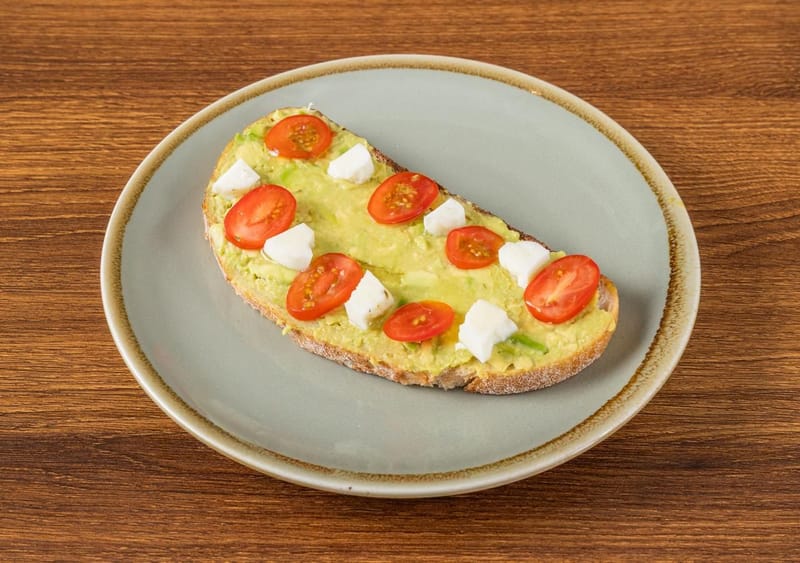 Sourdough topped with smashed avocado, halved cherry tomatoes and cubes of white cheese on a sage plate